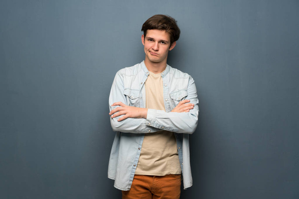 Adolescente hombre con chaqueta jean sobre gris pared sensación de disgusto
 - Foto, imagen