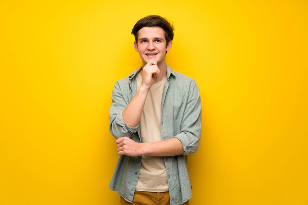 Adolescente hombre sobre la pared amarilla sonriendo y mirando hacia el frente con cara confiada
 - Foto, imagen