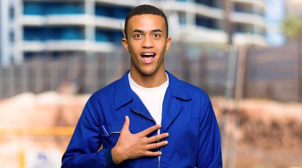 Νέος afro Αμερικανός εργαζόμενος άνθρωπος έκπληκτος και σοκαρισμένος ενώ ψάχνει δεξιά σε ένα εργοτάξιο - Φωτογραφία, εικόνα