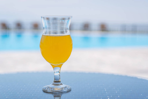glass of fresh orange or pineapple juice by the poolside - Фото, изображение