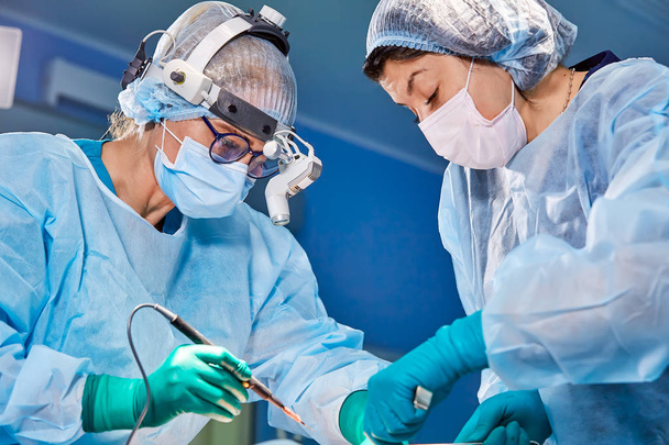 Retrato de un cirujano de cerca. Los cirujanos operan a un paciente. Caras tensas y serias. Operación real. Atmósfera tensada en quirófano
. - Foto, Imagen