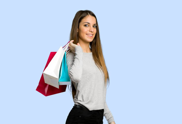 young girl holding a lot of shopping bags on blue background - Photo, Image