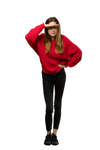eine Ganzkörperaufnahme einer jungen Frau mit rotem Pullover, die mit der Hand weit weg schaut, um etwas über einen isolierten weißen Hintergrund zu sehen - Foto, Bild