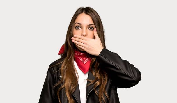 Jonge vrouw met lederen jas die betrekking hebben op mond met handen zeg iets ongepast over geïsoleerde grijze achtergrond - Foto, afbeelding