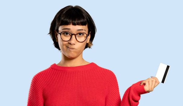 Short hair girl with red sweater taking a credit card without money on isolated blue background - 写真・画像