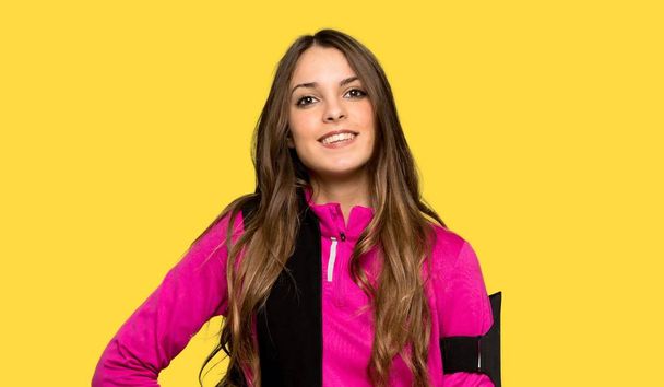 Young sport woman posing with arms at hip and smiling over isolated yellow background - Photo, Image