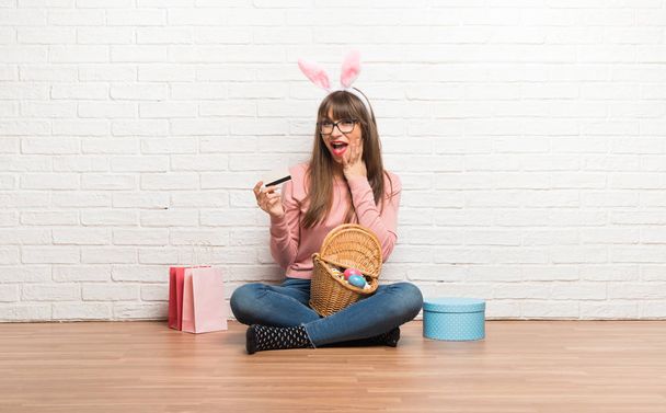 Γυναίκα με τα αυτιά λαγουδάκι για το Πάσχα διακοπές κάθεται στο πάτωμα κρατώντας μια πιστωτική κάρτα και εξέπληξε - Φωτογραφία, εικόνα