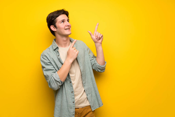 Teenager man over yellow wall pointing with the index finger and looking up - Foto, Bild