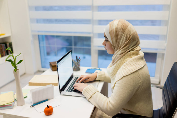 Young Muslim girl working on laptop at home office - 写真・画像