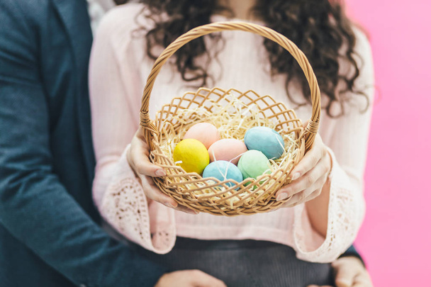 Couple on pink background. Close-up of an Easter basket with colorful eggs. The grip holds the basket in his hands and has a beautiful long hair. - Zdjęcie, obraz