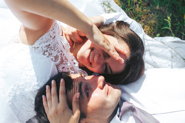 The bride and groom lie on a green meadow and bask in the sun - Photo, image