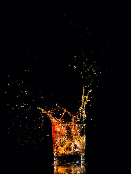 whiskey with splash on black background, brandy in a glass - Fotó, kép