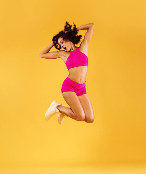 Strong athletic, woman, jumping on yellow background wearing sportswear. Fitness and sport motivation. - Fotó, kép