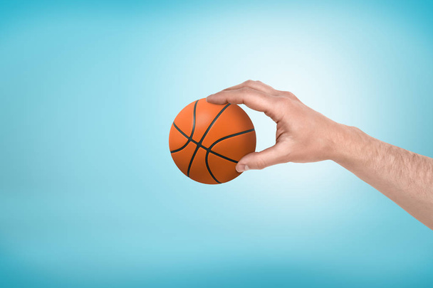 Side close-up of mans hand holding little basketball on light-blue background. - Фото, изображение