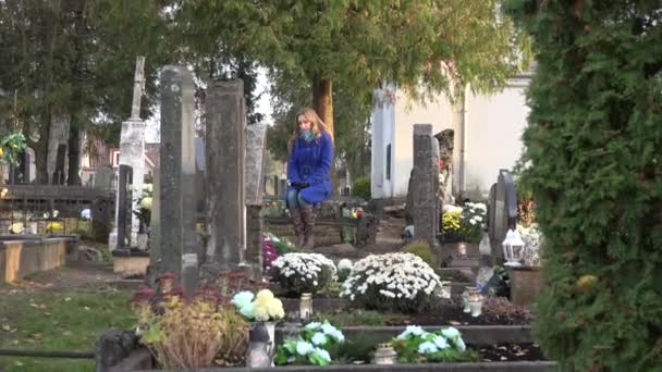 A mulher triste senta-se no banco perto da sepultura do marido pai no cemitério. Amplia. 4K
 - Filmagem, Vídeo
