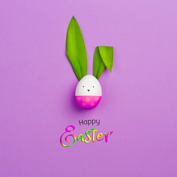 Easter Bunny made of colored egg and green leaves of spring flower on purple background. happy Easter text. minimalism, copy space - Photo, image