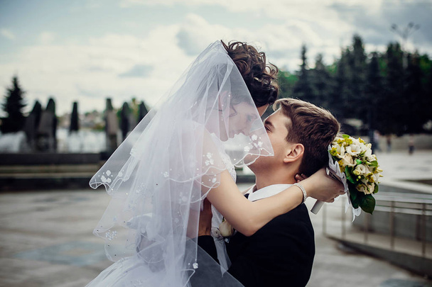 Happy groom holding a handsome wife in a white dress on the back - Foto, immagini