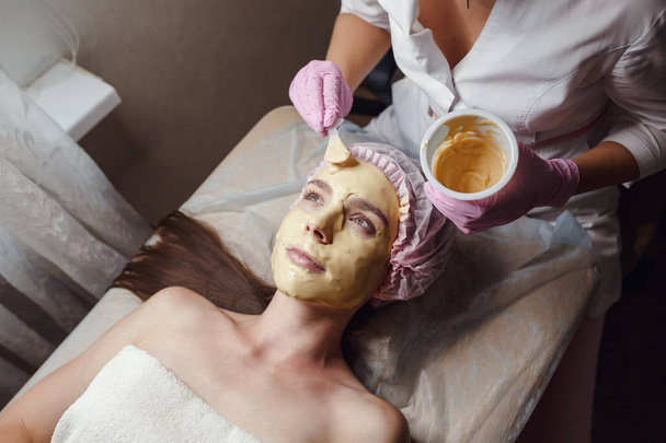Cosmetólogo haciendo procedimiento de belleza para el paciente. Peeling máscara de oro
 - Foto, Imagen