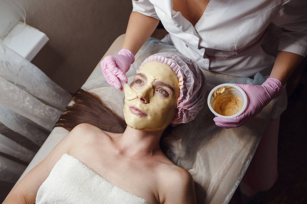 Ο αισθητικός κάνει διαδικασία ομορφιάς για τον ασθενή. Ξεφλούδισμα χρυσή μάσκα - Φωτογραφία, εικόνα