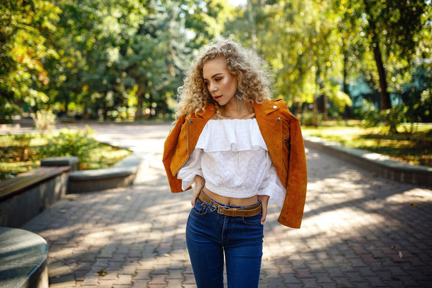 Uma bela jovem com cabelo encaracolado loiro caminha pela cidade ensolarada
 - Foto, Imagem