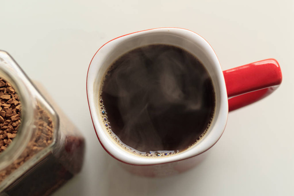 rode mok. koffie wordt gegoten in het. Hij is een echte stoom. Naast de glazen pot, worden koffie korrels geopend in het - Foto, afbeelding