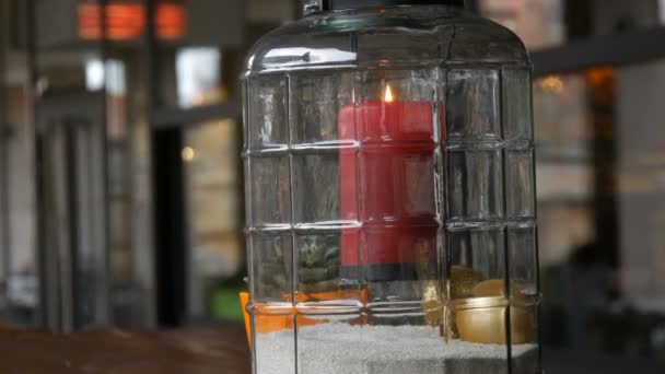 Beautiful glass candlestick with a big red burning wax candle of red color which is inside the candlestick and stands on the table of the street cafe - Footage, Video