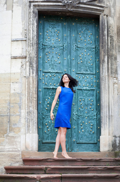 Молода дівчина позує у блакитній сукні для камери на фоні зелених металевих дверей. Впевнена стильна жінка дивиться в бік
 - Фото, зображення