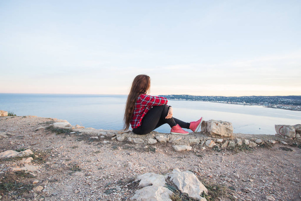 Podróży, przygody i pojęcie samotności - dziewczyna siedzi na skraju urwiska i patrząc na morze - Zdjęcie, obraz
