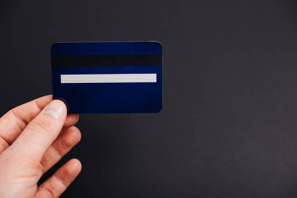 Ruka držící Modrou kreditní kartu na pozadí černá stěna - Fotografie, Obrázek