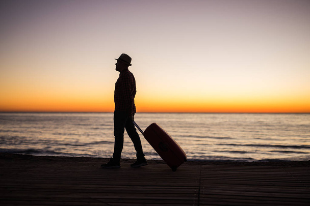 Tatil, yaz ve seyahat kavramı - genç adam siluet çanta batımında denize yakın - Fotoğraf, Görsel