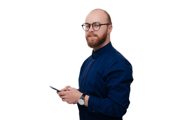 Profiilinäkymä onnellinen parrakas mies yllään lasit käyttäen mobiili hymyillen ja katsoen kameraa valkoisella taustalla
  - Valokuva, kuva
