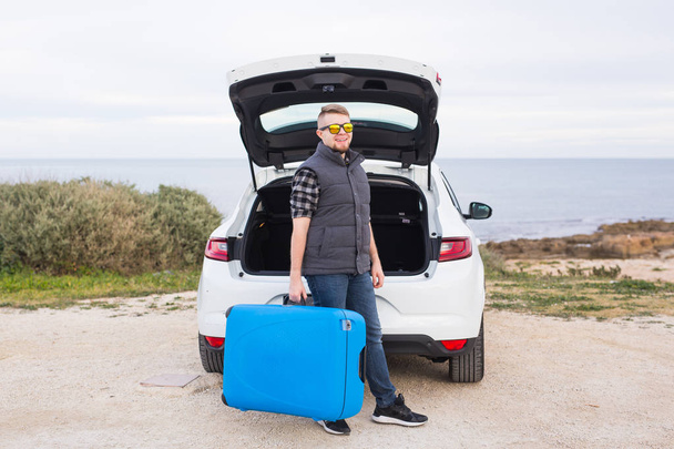 Travel, holidays and vacation concept - man near the car with blue suitcase - Zdjęcie, obraz