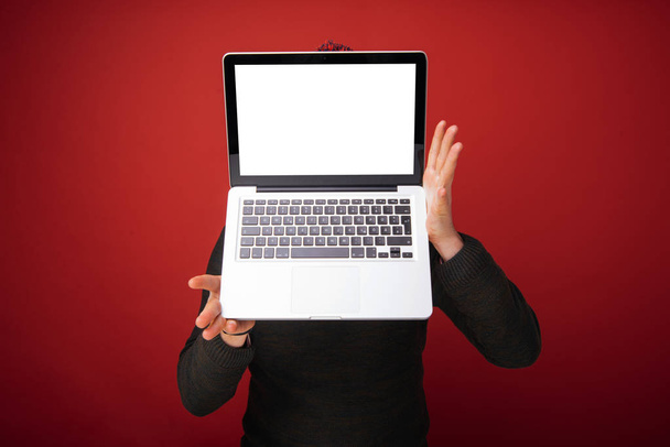 Hombre guapo de pie ove fondo rojo y mostrando el ordenador portátil delante de su cara
  - Foto, imagen