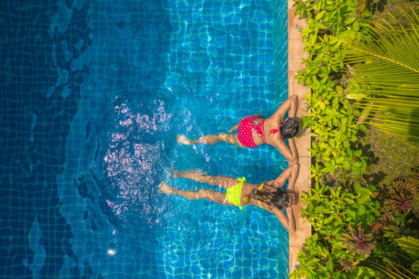 Luchtfoto bovenaanzicht boven zwembad. vrouw in een gele bikini en vrouw in rode bikini zijn zwemmen - Foto, afbeelding