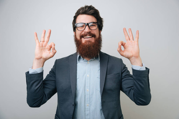 Gros plan portrait jeune beau, heureux, souriant, homme barbu, employé d'entreprise, travailleur donnant OK signe avec les doigts adn les deux mains
  - Photo, image