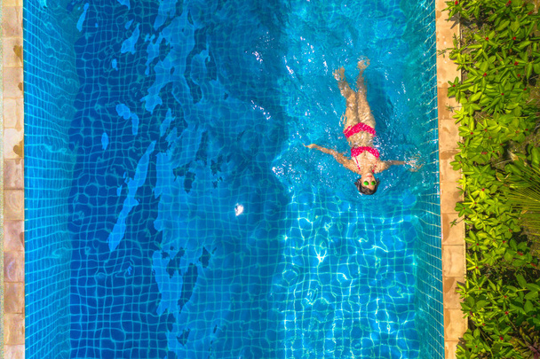 赤いビキニの空中トップビューの女性は、ヴィラプールで泳いでいます - 写真・画像