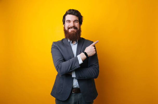 Smiling business man which pointing away and looking at camera. Isolated yellow background - Photo, Image