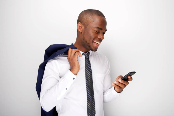 Retrato lateral del joven hombre de negocios afroamericano mirando el teléfono celular por la pared blanca
 - Foto, Imagen
