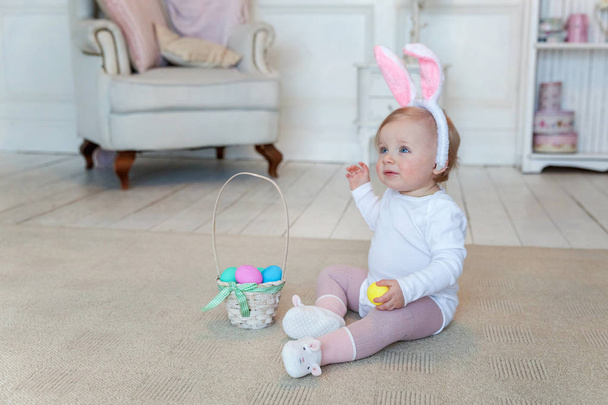 kleines Mädchen trägt Osterhasenohren und spielt mit bemalten Eiern - Foto, Bild