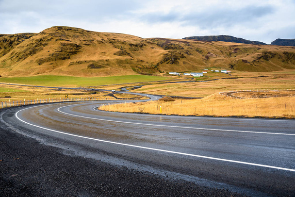 Обводнение мокрой горной дороги в Исландии в пасмурный день. На заднем плане видна ферма у подножия горы
. - Фото, изображение