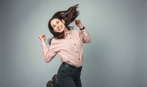 Porträt einer fröhlichen jungen Frau, die Erfolg feiert, während sie isoliert über grauen Hintergrund springt  - Foto, Bild