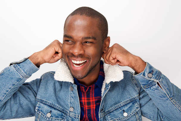 Primer plano retrato de fresco joven afroamericano modelo de moda masculina sonriendo con chaqueta de mezclilla contra la pared blanca
 - Foto, Imagen