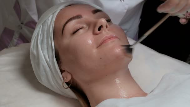 Retrato de una hermosa chica en el procedimiento en el salón de belleza. Primer plano. Un cosmetólogo-terapeuta aplica un gel transparente a la cara de los clientes para reducir las arrugas y rejuvenecer la piel femenina
. - Imágenes, Vídeo