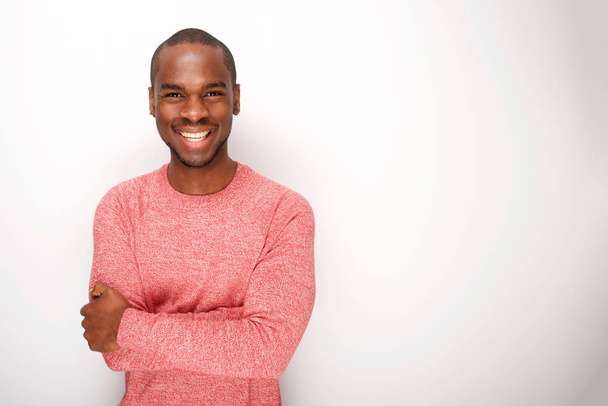 Porträt eines modischen jungen schwarzen Mannes, der mit von weißer Wand verschränkten Armen lächelt - Foto, Bild