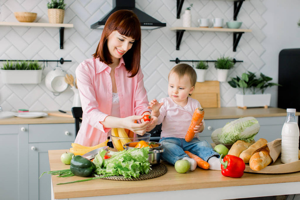 mother preparing salad for dinner and showing kid tomatoes in kitchen - Foto, imagen