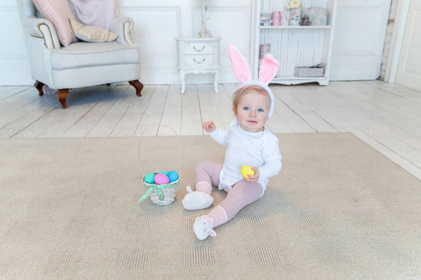 Pieni lapsi tyttö yllään pupu korvat pääsiäispäivänä ja leikkii maalattu munia
 - Valokuva, kuva