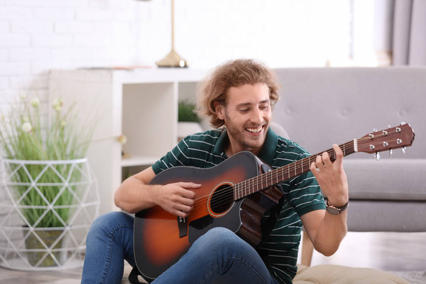 Young man playing acoustic guitar in living room - Fotó, kép