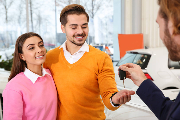 Car salesman giving key to couple in dealership - Foto, afbeelding