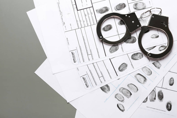 Handcuffs and fingerprint record sheets on grey background, space for text. Criminal investigation - Photo, Image
