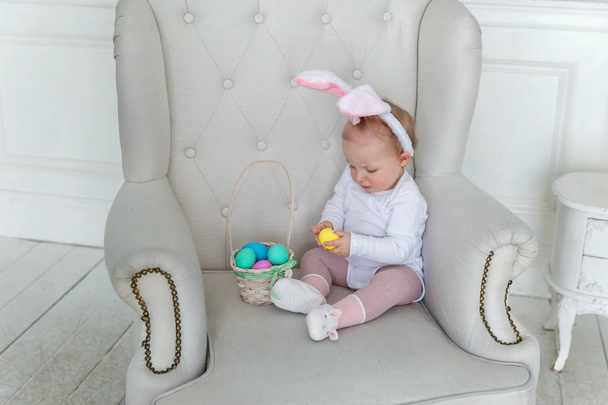 Niña pequeña con orejas de conejo el día de Pascua y jugando con huevos pintados
 - Foto, Imagen